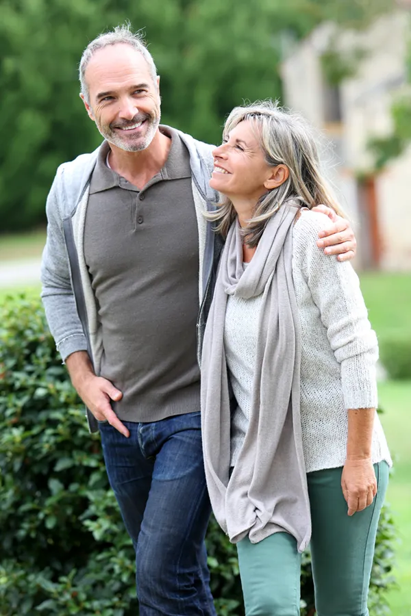Bioidentical-Hormone-Therapy-Treatment A mature couple in gray toned clothes and jeans walk happily outside, happy with their successful bioidentical hormone treatments from Lux Hormones & Health Wellness in San Diego.