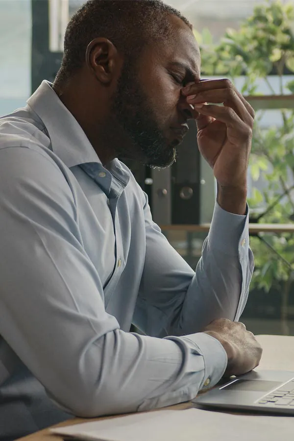 Chronic-Fatigue-Treatment A black man rubbing the top of his nose at his desk, in need of chronic fatigue treatment from Lux Hormones & Health Wellness in San Diego.