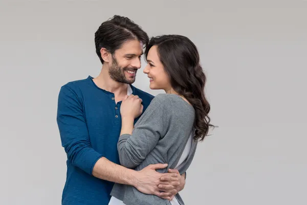 Erectile-Dysfunction-Doctor A man in a blue shirt embracing a woman in a gray shirt smiles due to his successful erectile dysfunction care from Lux Hormones & Health Wellness in San Diego.