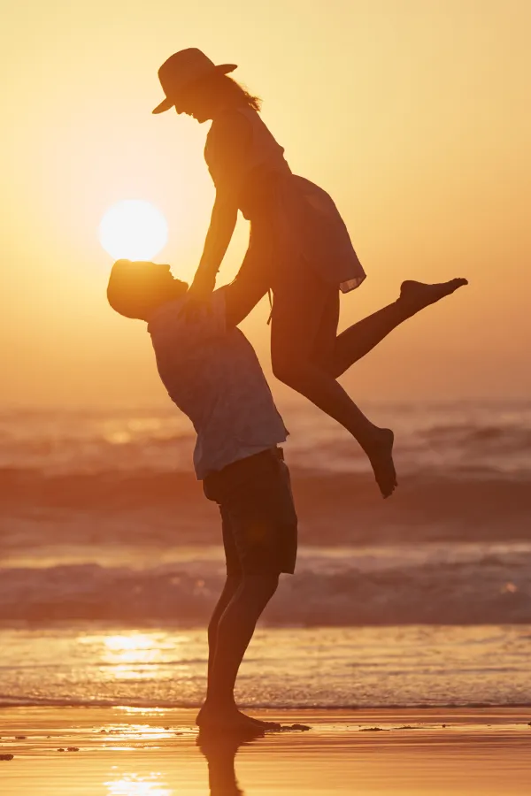 LCL-Tears-Treatment A man lifts a woman into the air on the beach. Get treatment for LCL tears from Lux Hormones & Health Wellness in San Diego.