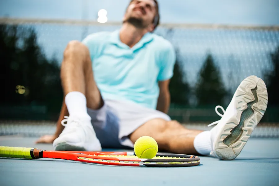 LCL-Tears-and-Knee-Pain-Clinic A tennis player grimacing in pain sits on the court, extending a leg with a knee injury. Schedule regenerative medicine for LCL tears and knee pain from Lux Hormones & Health Wellness in San Diego.