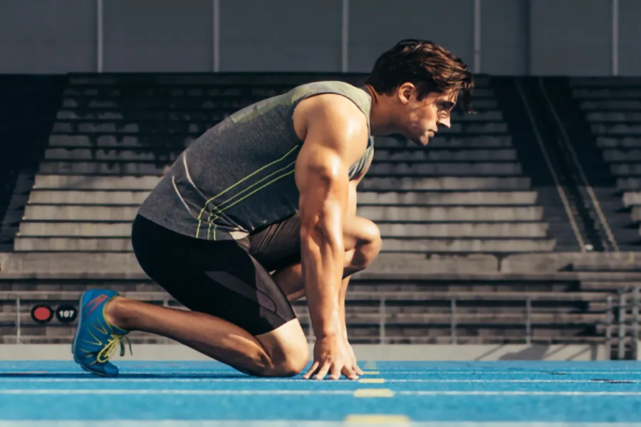 Lean-Muscle-and-Recovery-Clinic A white man kneels at the starting line on a track, determined to do his best. Get treatment for lean muscle loss and recovery from Lux Hormones & Health Wellness in San Diego.