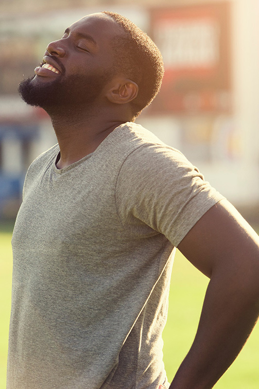 Lean-Muscle-and-Recovery-Treatment A black man in a gray t-shirt and smiles, looking up with closed eyes after a satisfying workout. Get treatment for lean muscle loss and recovery from Lux Hormones & Health Wellness in San Diego.