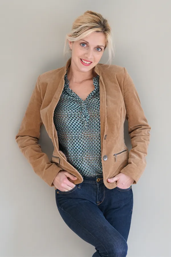Metabolic-Syndrome-Treatment A smiling blonde woman in a tan leather jacket leans against a gray wall. Schedule metabolic syndrome from Lux Hormones & Health Wellness in San Diego.