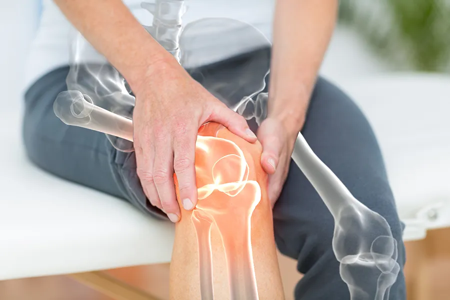 Osteoarthritis-Clinic A 3D illustration of the skeleton over the body of a woman who holds her knee in pain, where the area is highlighted. Schedule osteoarthritis treatment from Lux Hormones & Health Wellness in San Diego.