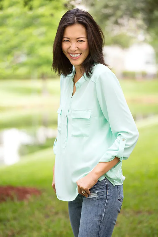 Perimenopause-Treatment A middle-aged brunette woman in a light green button-up shirt stands outside smiling, happy with her perimenopause treatment from Lux Hormones & Health Wellness in San Diego.